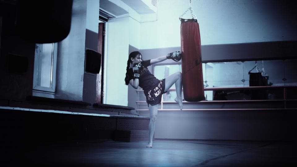 A woman kicking a heavy bag in a dim training room