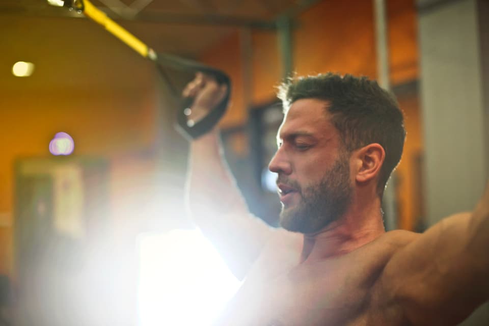 A man pulling on suspension straps in a warmly lit gym