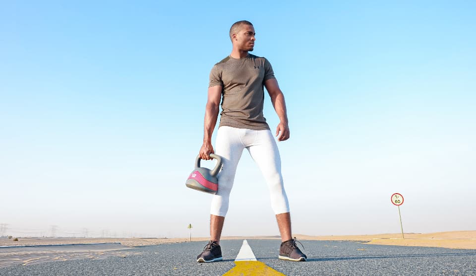 A man holding a kettlebell outdoors under a blue sky