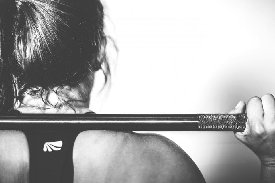 A woman with a barbell across her shoulders, ready to squat